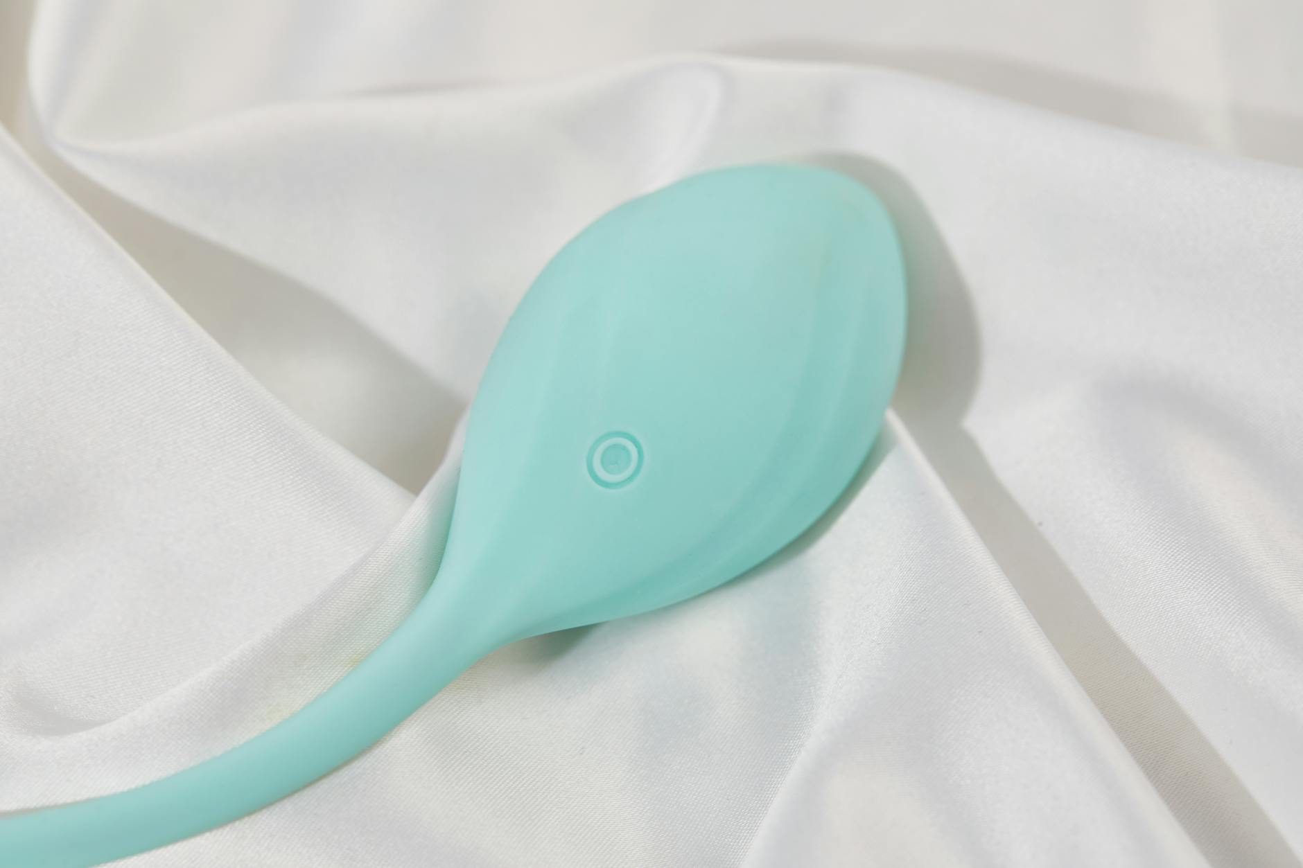 A stylish teal vibrator on smooth white silk fabric, symbolizing pleasure and relaxation