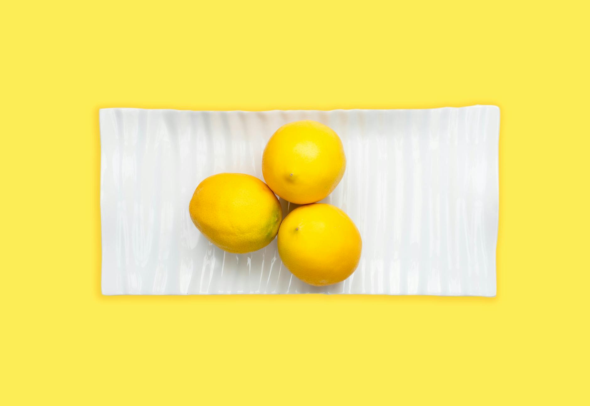 Fresh lemons arranged on a white plate with a vibrant yellow background, symbolizing freshness and the lemon vibrator brand