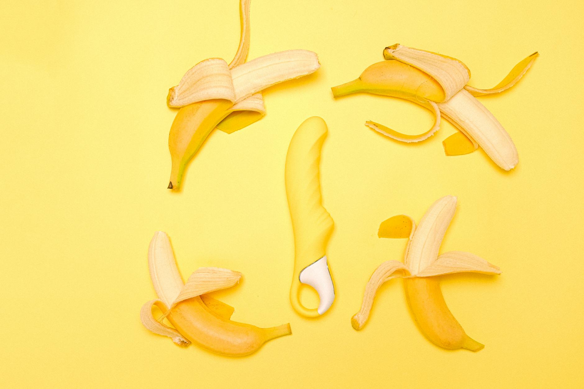 A bright yellow silicone clitoral vibrator nestled among fresh lemons on a yellow background.