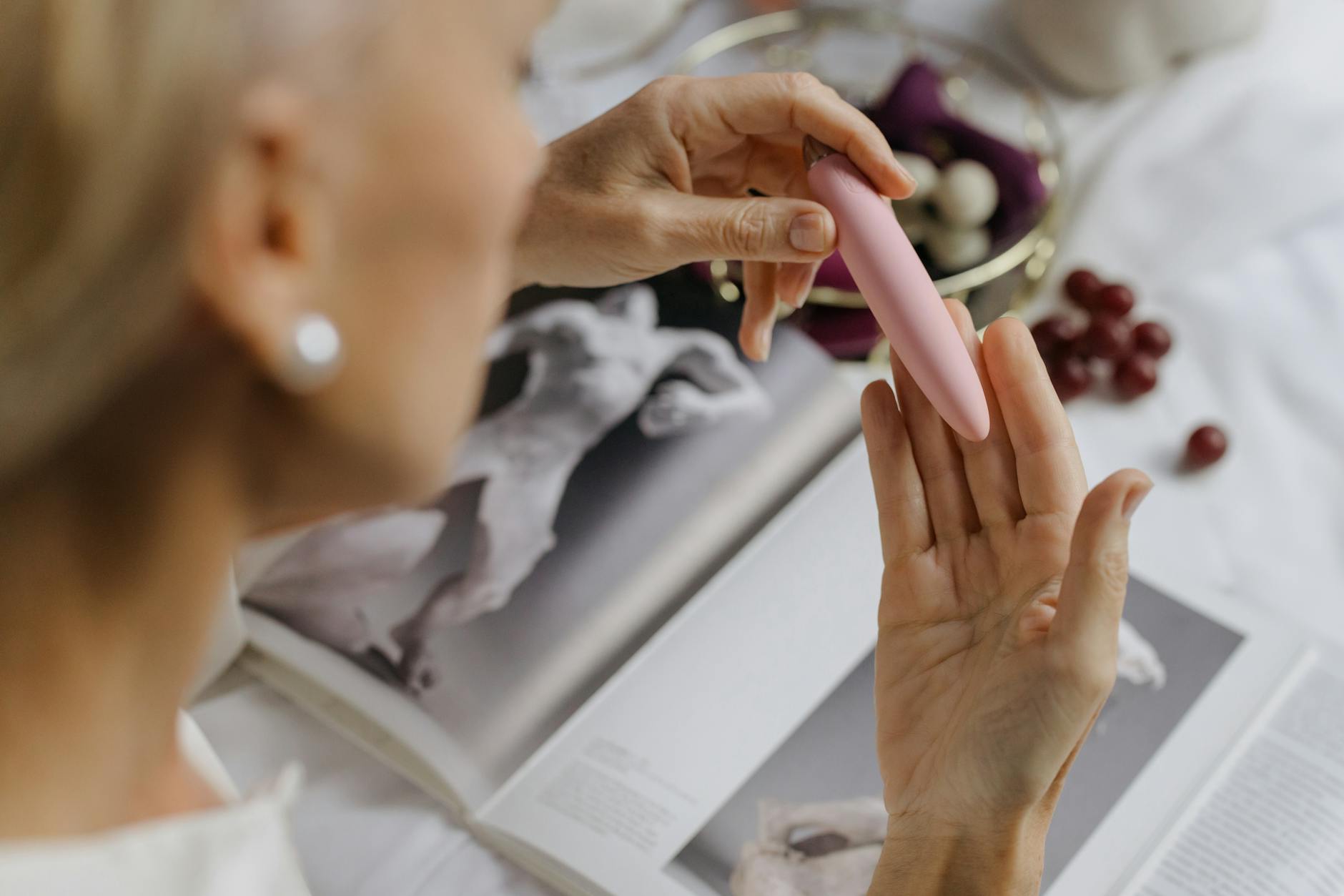 Close-up of hands holding a pink vibrator with books nearby, symbolizing intimate self-care and pleasure exploration.