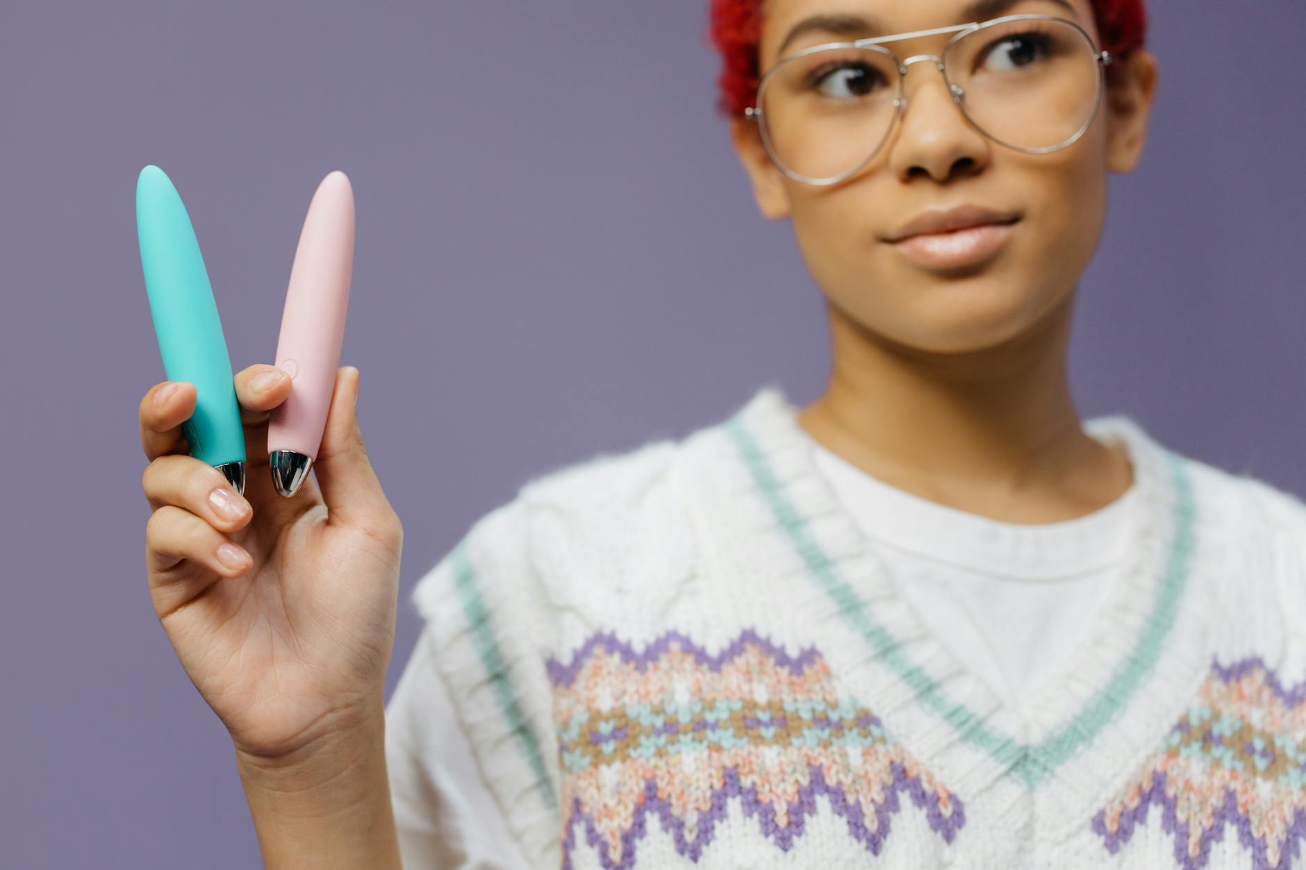Woman holding colorful vibrators against a purple background, representing diverse pleasure solutions