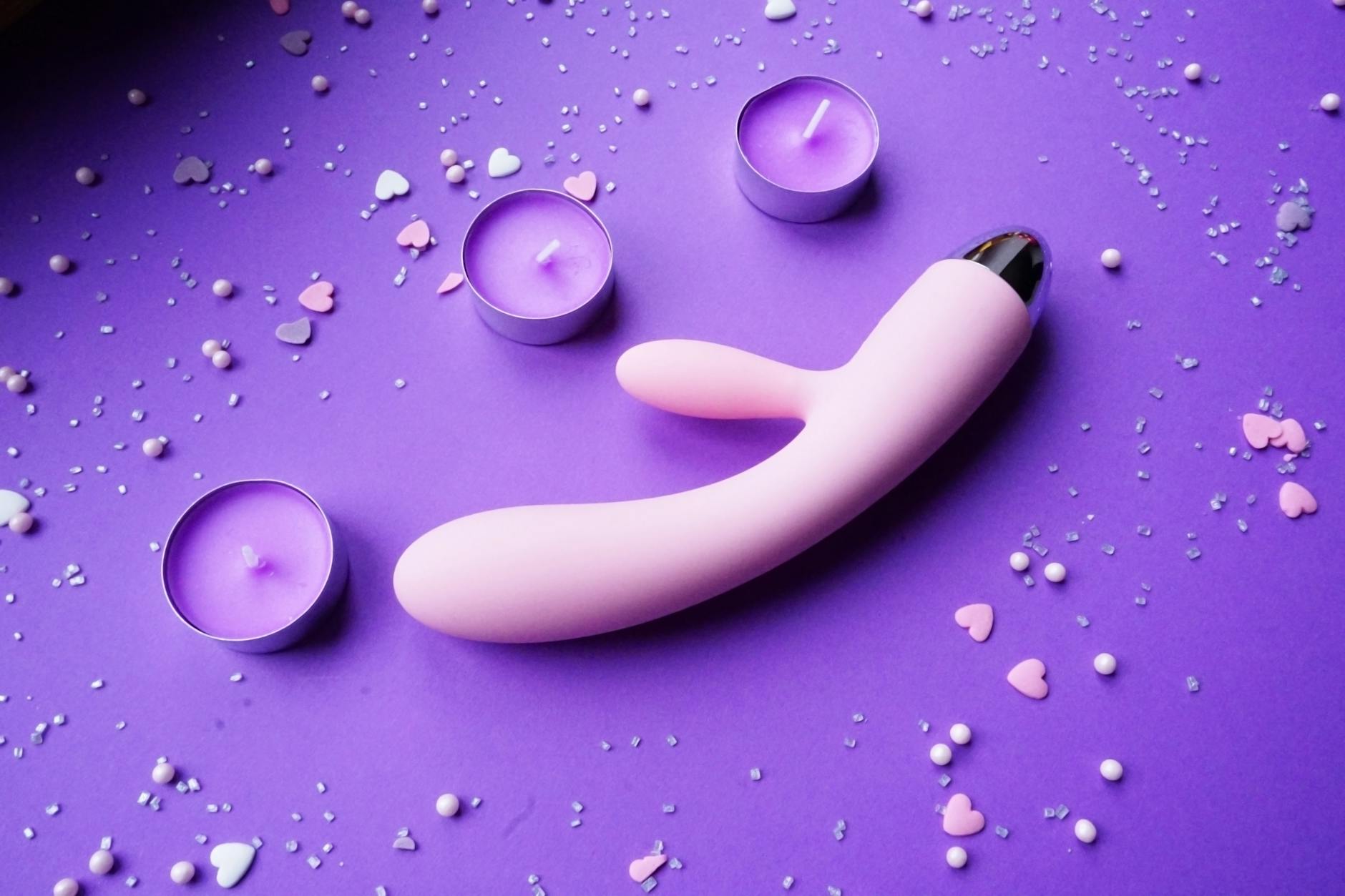 Pink lemon vibrator on purple background with heart confetti and candles for romantic ambiance