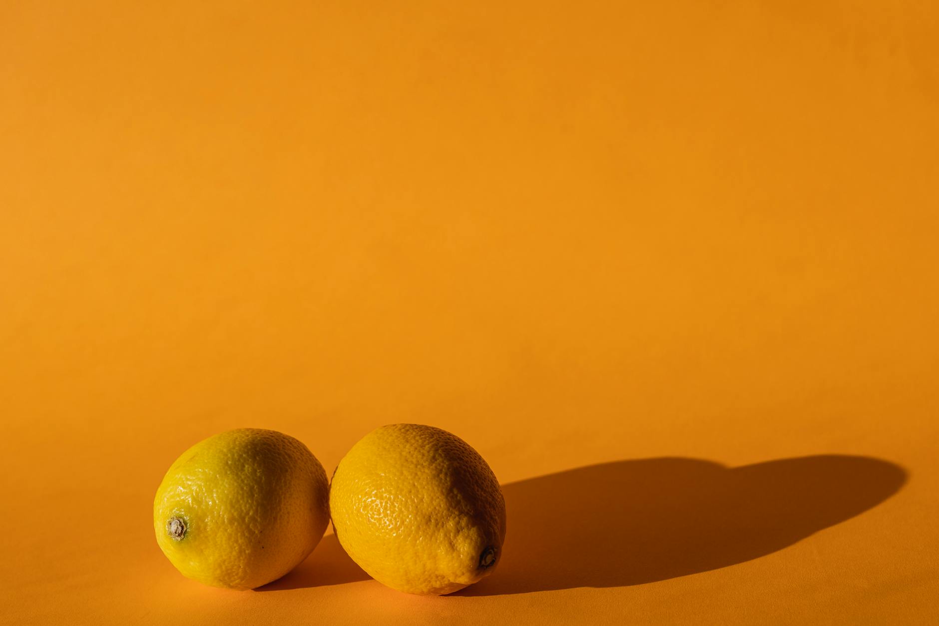 Hand holding a fresh lemon on soft pink background with additional lemons nearby